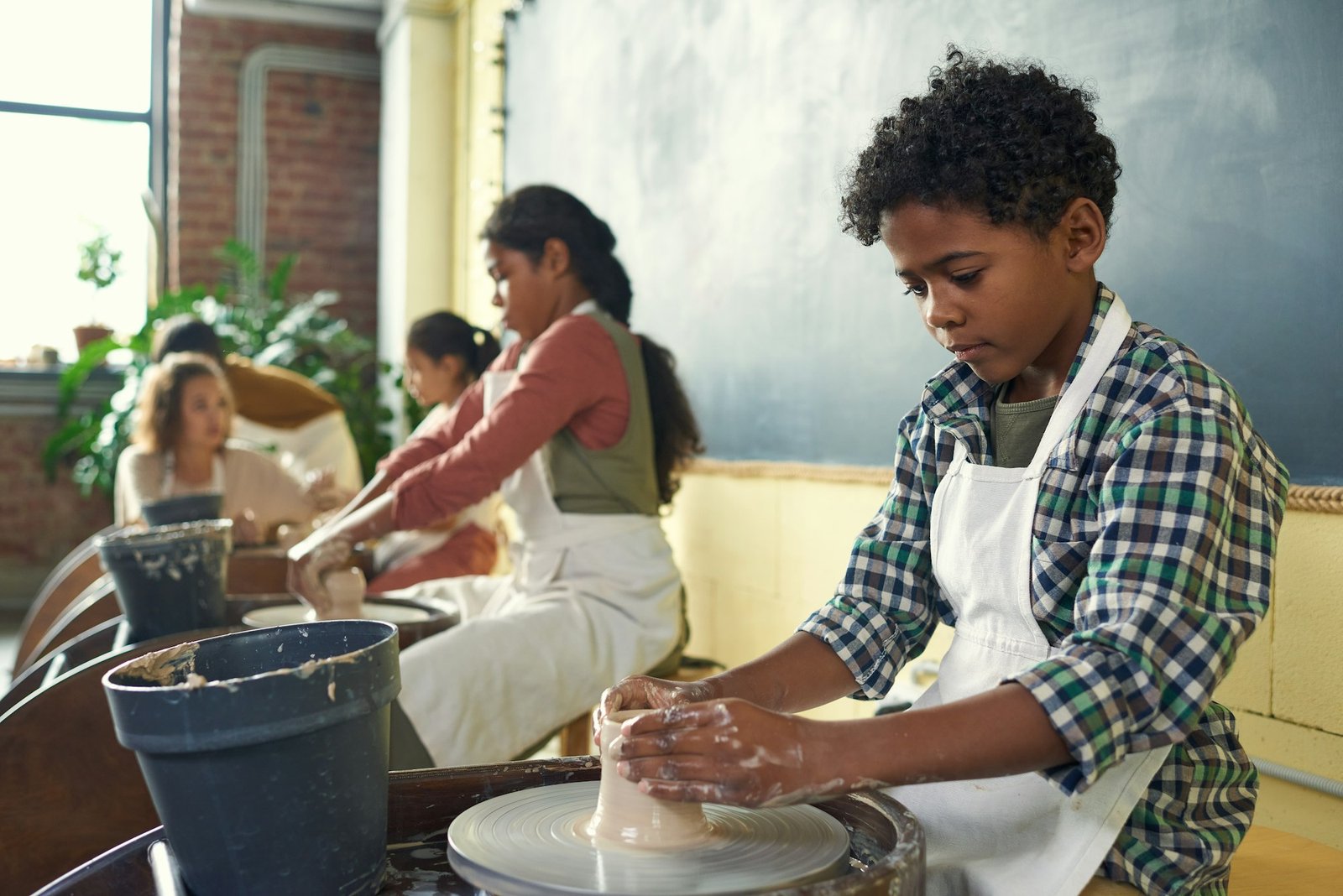 Cute African schoolboy in apron sculpting earthenware