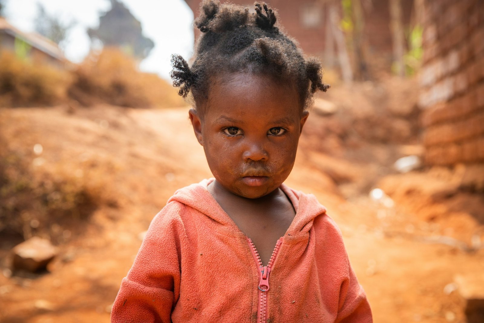Poor little girl wearing dirty clothes in an African village, poverty and crisis concept.